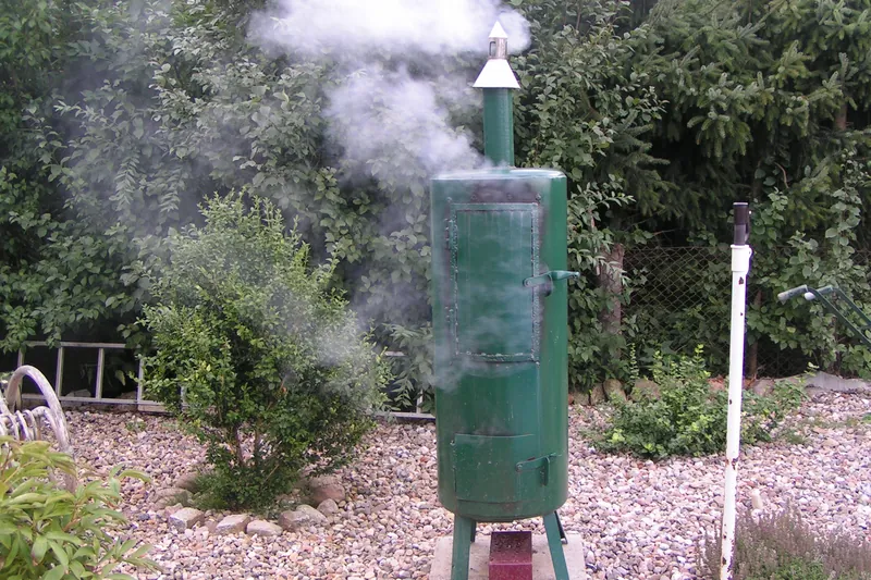 Grüner Räucherofen aus Metall im Garten, aus dem Schornstein steigt Rauch